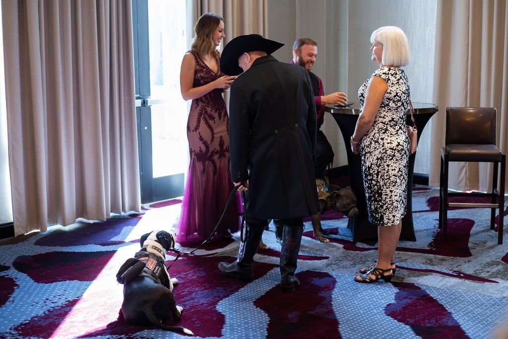 A formal gathering in a room with patterned carpet, featuring four people, a dog, and a person in a formal hat and coat.