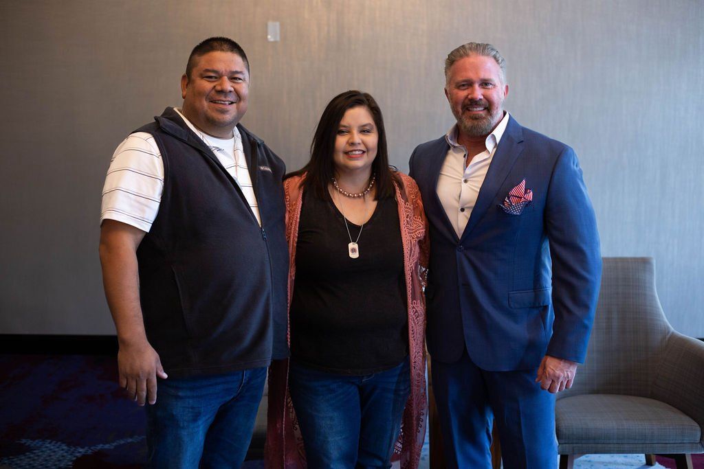 Three people smiling and posing for a photo indoors against a neutral wall.