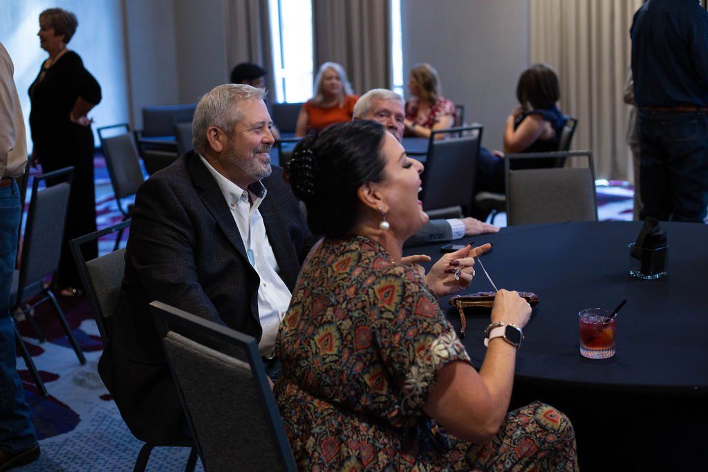 A group of people sitting at tables in a conference room, laughing and conversing during an event.