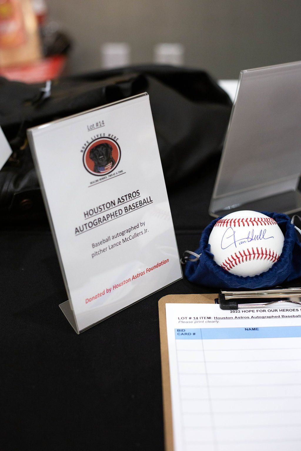 A sign for a Houston Astros autograph baseball auction sits next to a signed baseball and a clipboard on a black table.