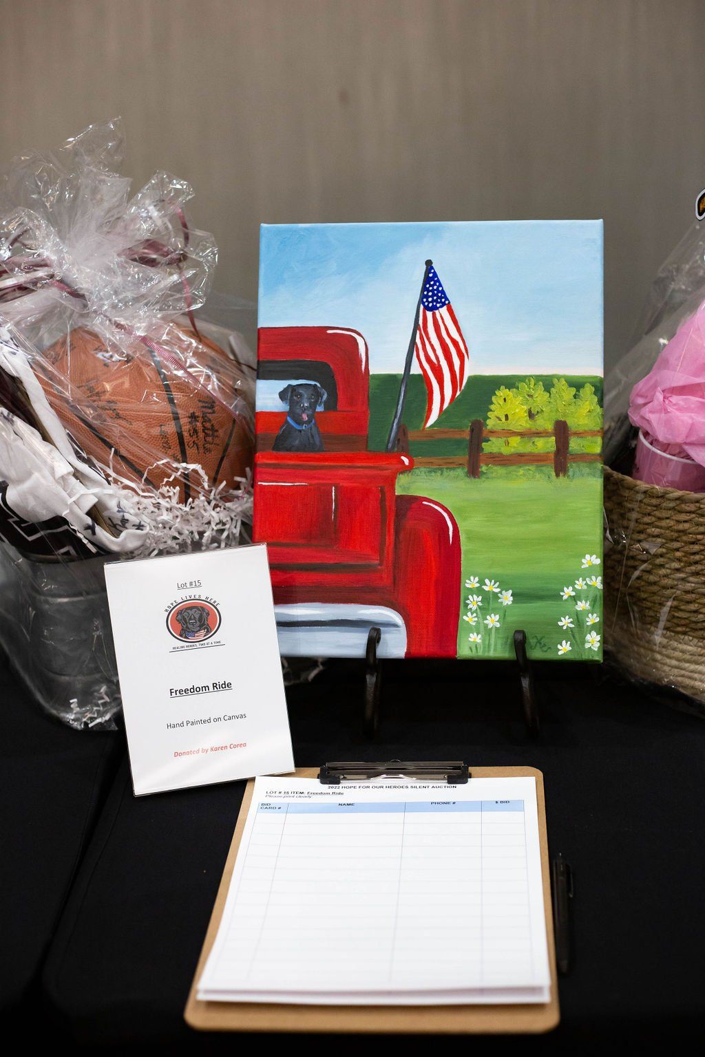 A silent auction display featuring a painting of a red truck with a dog and American flag, a basketball basket, and a sign.