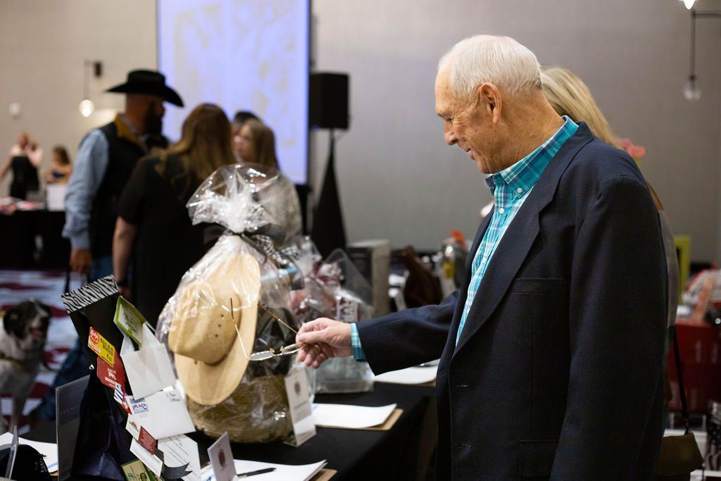An individual in a navy blazer examines gift baskets on a table at a brightly lit indoor event.