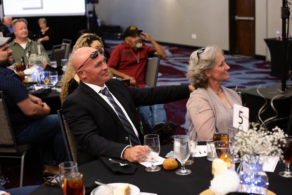 A man in a suit and a woman at a banquet table sit together, both looking off to the side during an event.