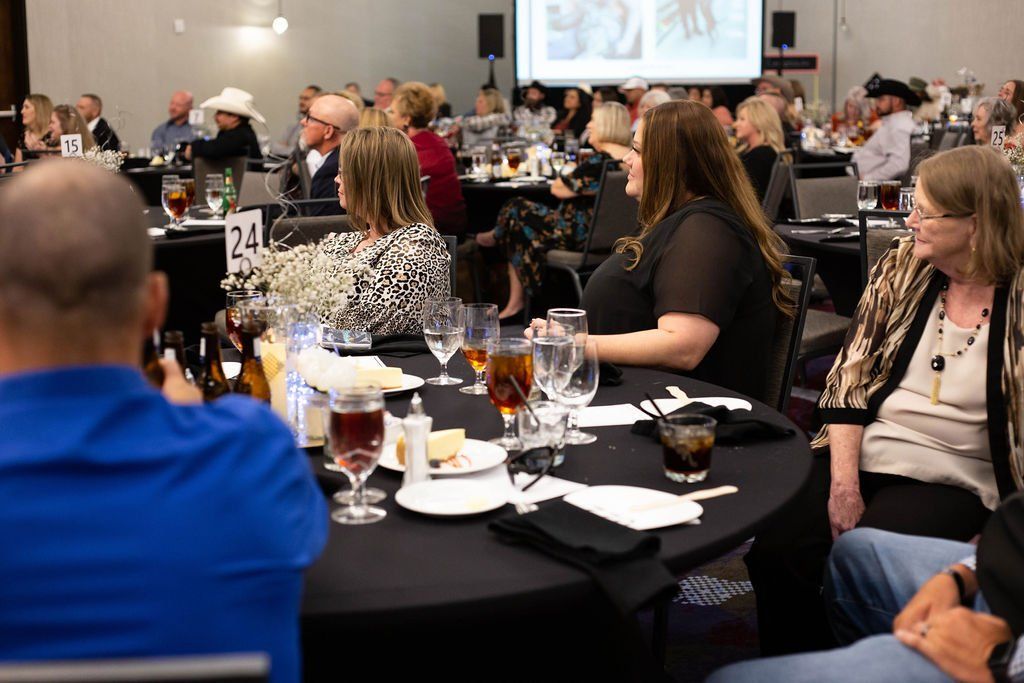 Attendees at tables in a dimly lit banquet hall face a projection screen during a seated dinner event.