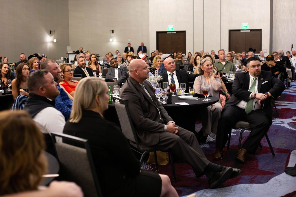 Audience members seated at tables in a conference room listening to a presentation.