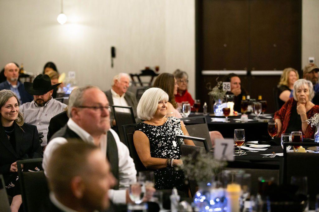 Guests seated at tables in a dimly lit banquet hall, listening to a speaker during an event.