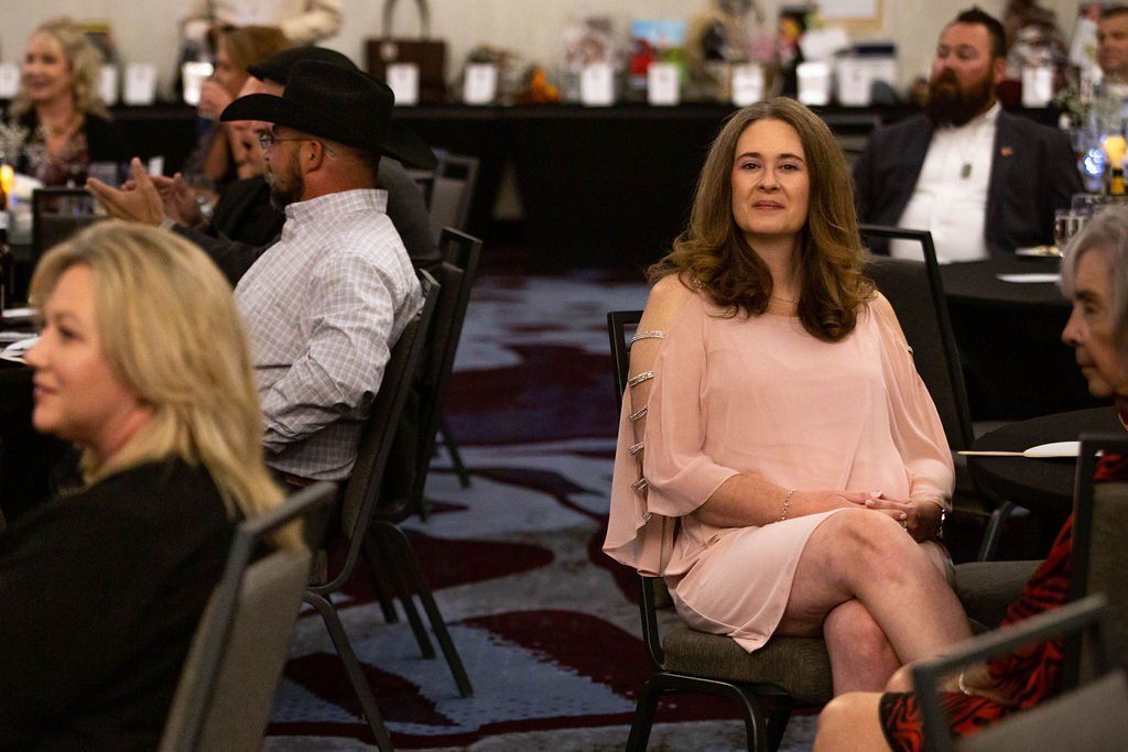 People seated at tables in a ballroom setting, focusing on a woman in a pink dress sitting in the foreground.