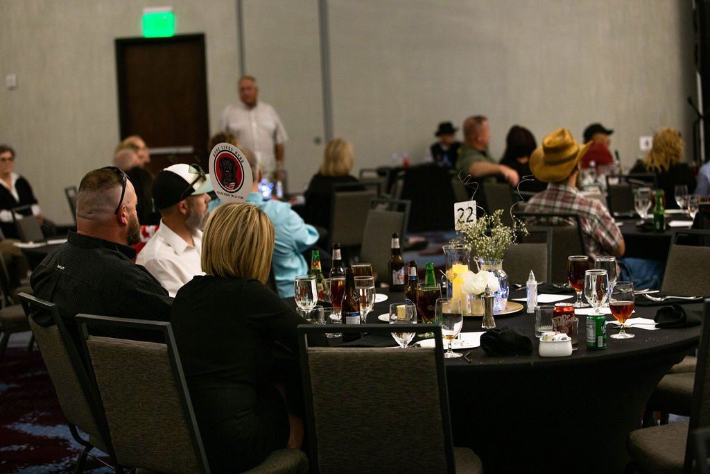 People seated at round tables in a conference room, listening to a person standing at the front of the room.