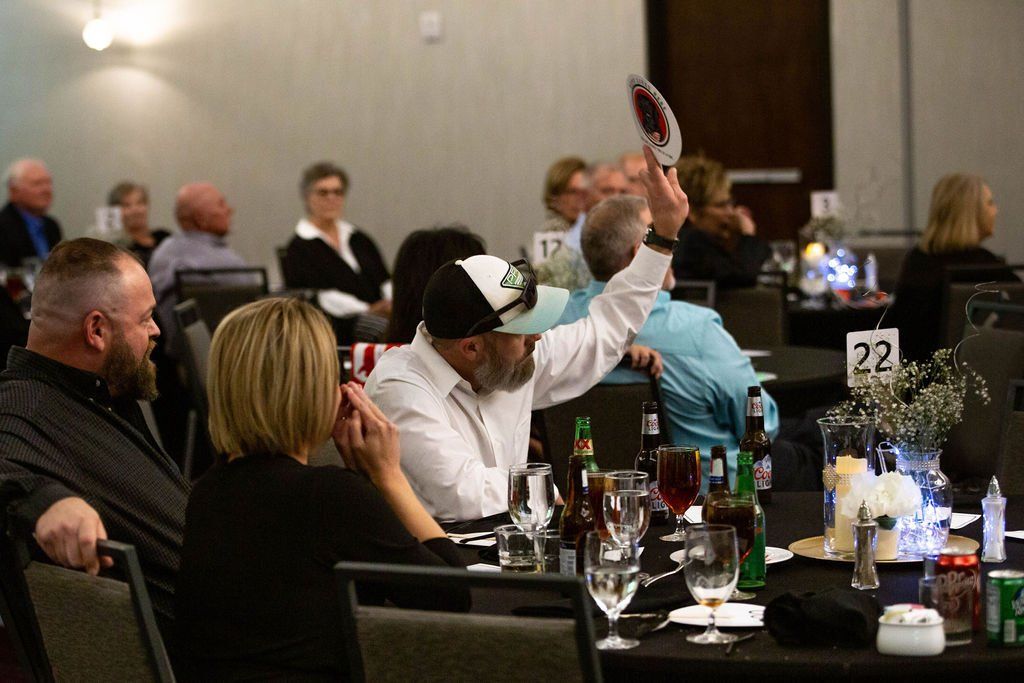 A person holding up an auction paddle at a table during a banquet, surrounded by seated guests.