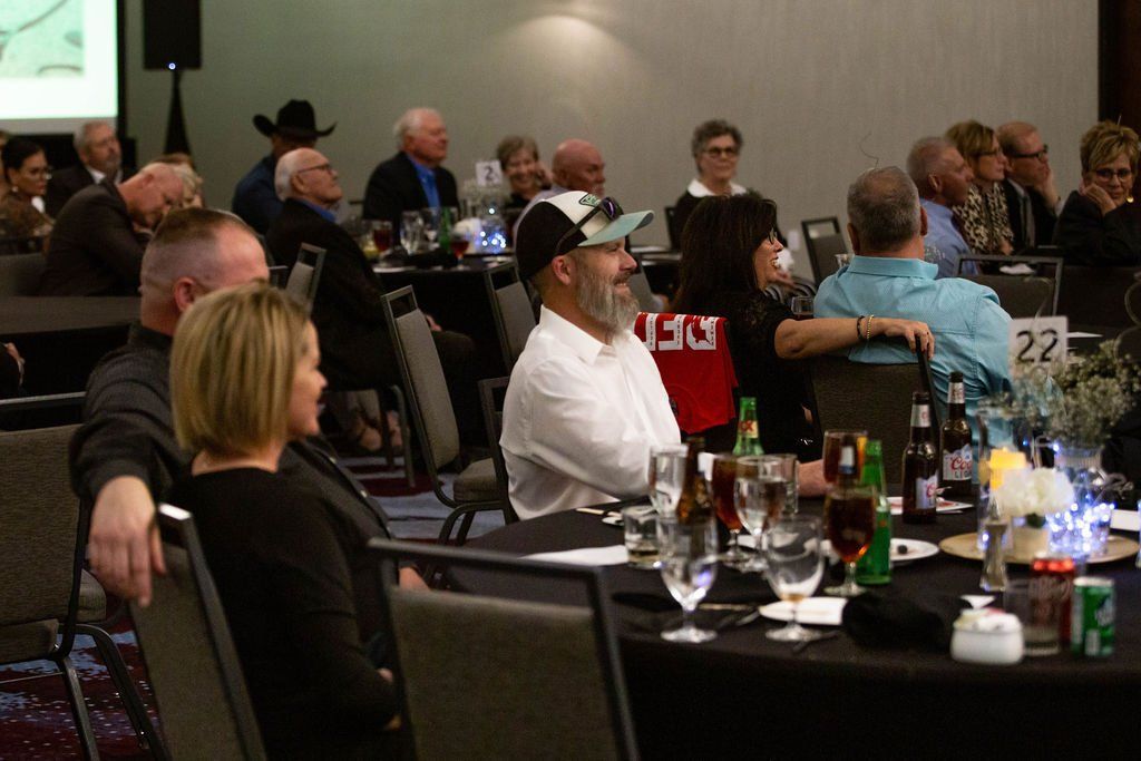 Attendees sit at circular tables at a conference, listening to a presentation.