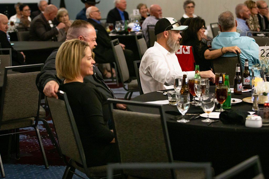People sit at tables with drinks in a banquet hall, with a couple in the foreground facing the event.