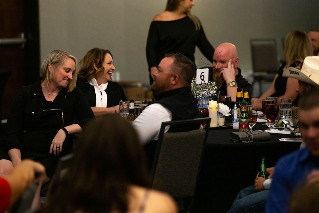 A group of people laughing and talking at a table during a social event in a dimly lit room.
