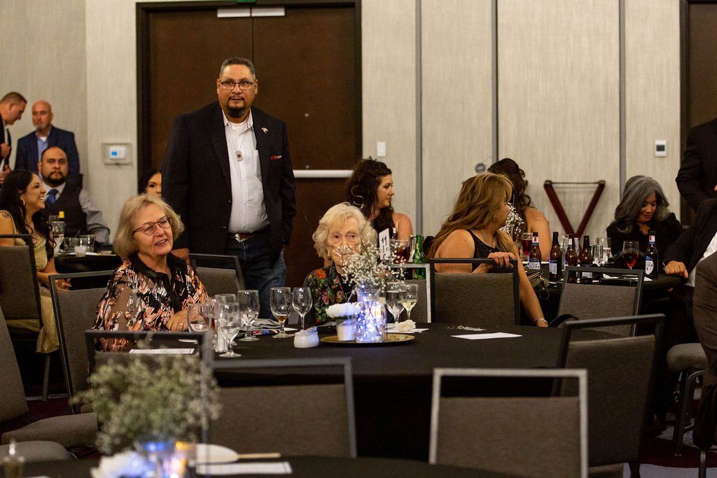 A man standing in a banquet hall while guests are seated at round tables for an event.