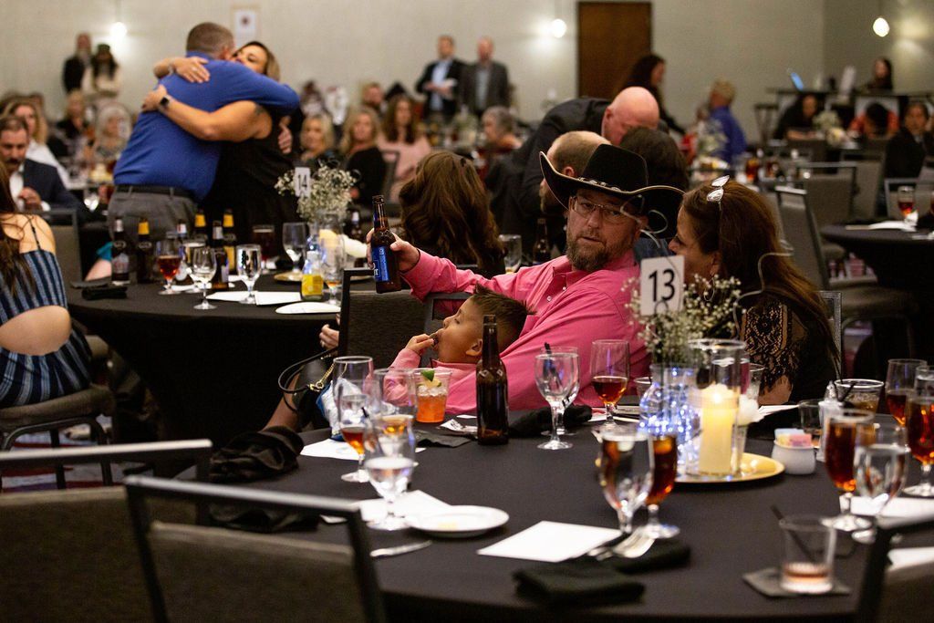 A ballroom banquet scene featuring a man in a pink shirt and cowboy hat sitting at table 13, with guests socializing.