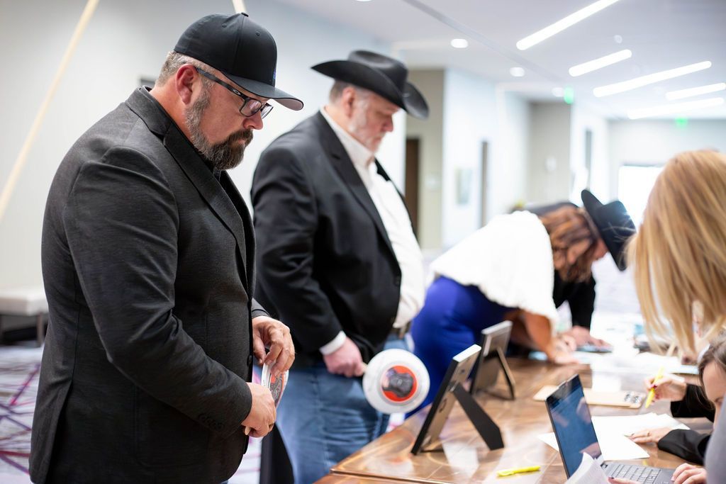 Attendees in business casual and formal attire stand at a table to sign documents in a brightly lit indoor venue.