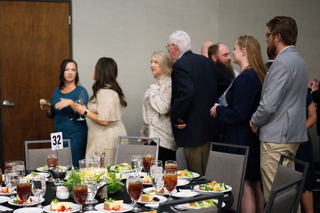 A group of people standing in a line at a catered event with tables set for a meal.