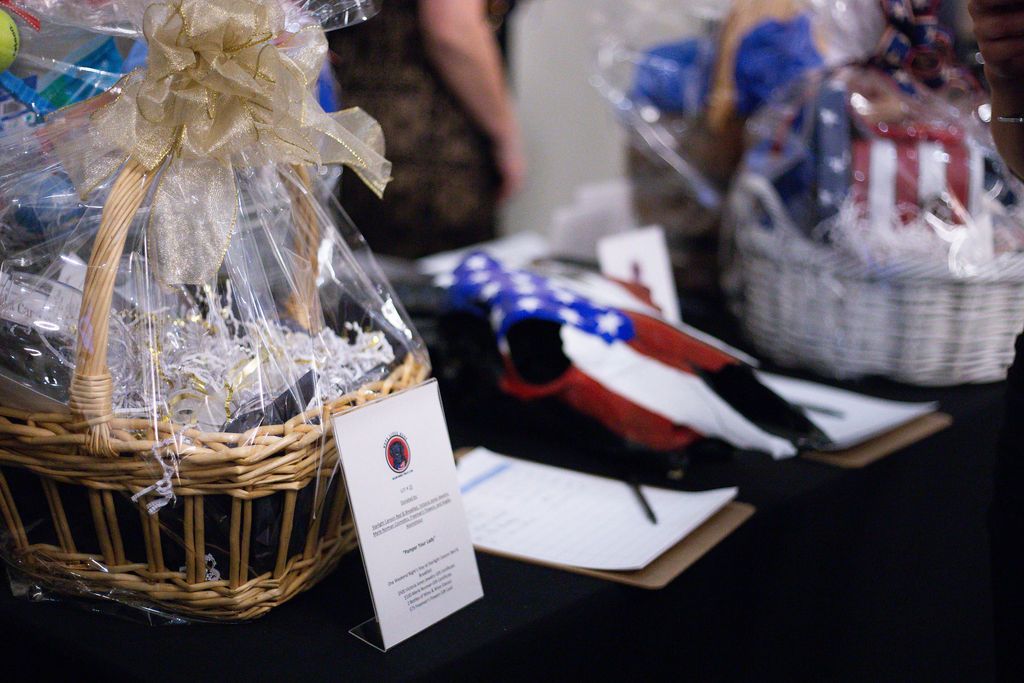Gift baskets with wrapped items and bid sheets placed on a table for an auction.