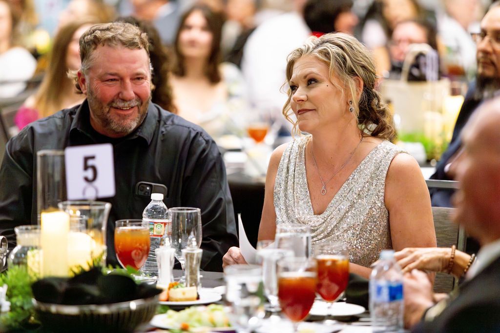 A man and woman sit at a dinner table marked with the number 5, both smiling while looking toward a person off-camera.