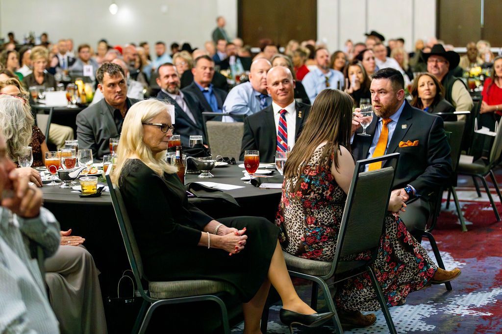Attendees seated at round tables in a large event space, engaged in conversation during a formal gathering.