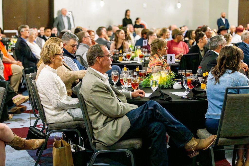 People seated at round tables in a brightly lit banquet hall, attending a professional conference or formal gathering.