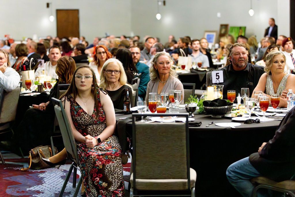People seated at tables in a brightly lit banquet hall, attending an event with drinks and formal place settings.