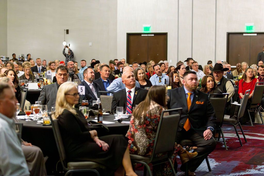 A large audience seated at tables in a conference room, listening to a presentation.