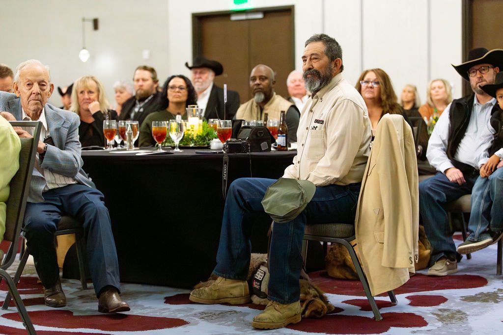 A group of people sit at tables in a conference room, listening attentively to a presentation.
