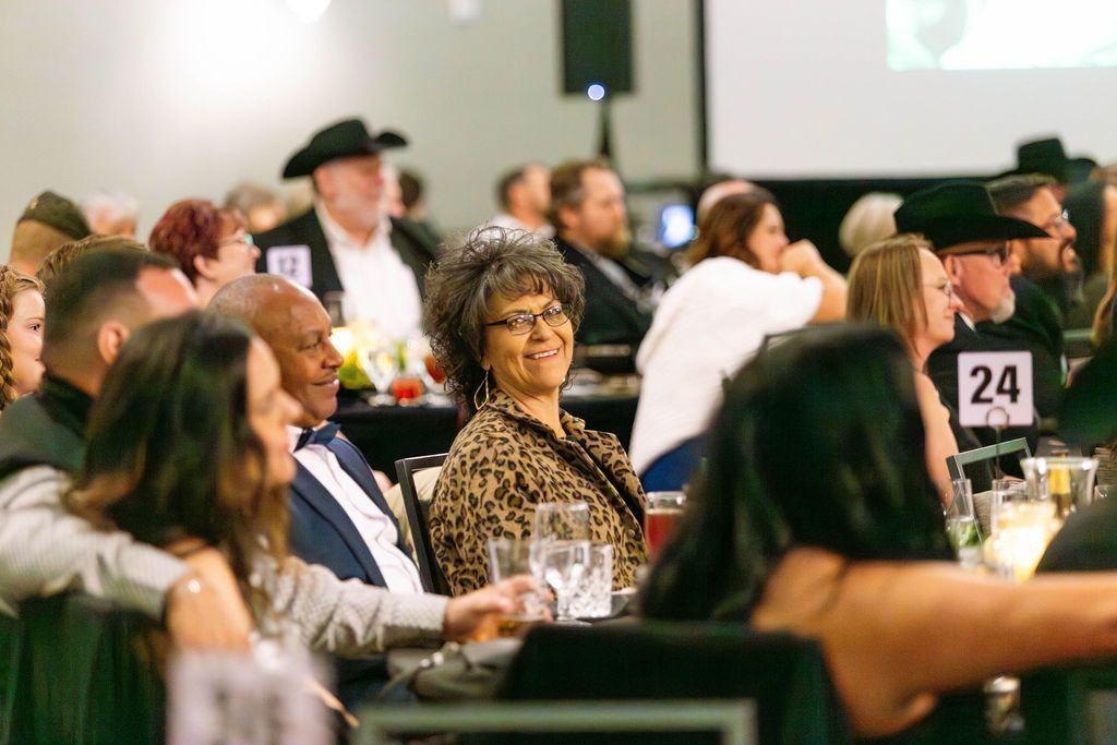 People at round tables in a banquet hall, with one smiling person wearing an animal print top looking towards the camera.