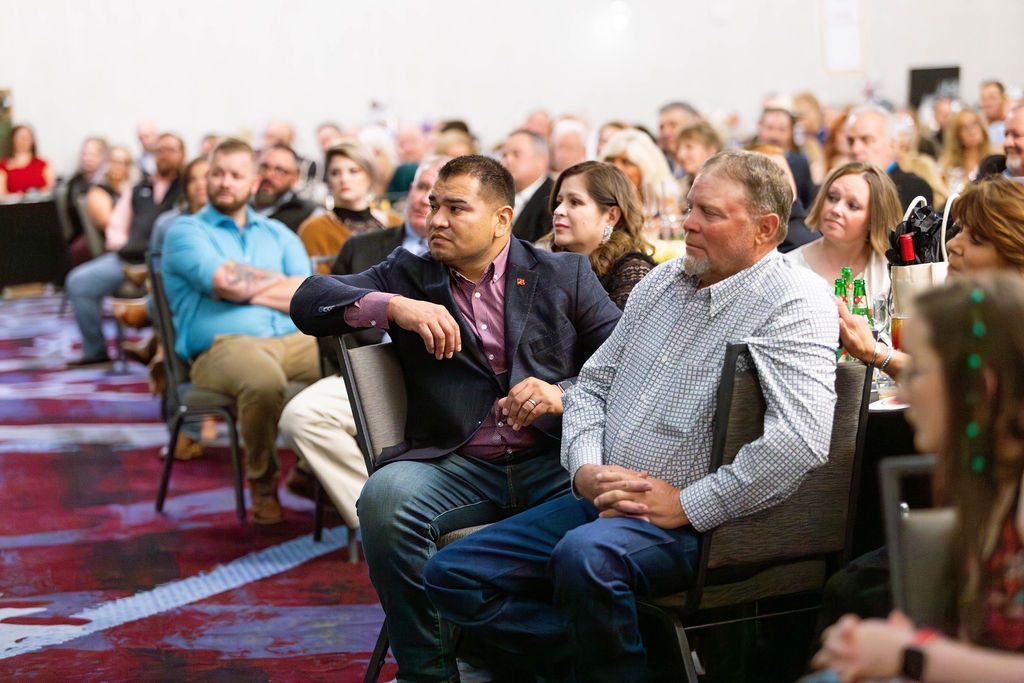 An audience seated in chairs at a conference or event, with attendees listening attentively in a brightly lit room.