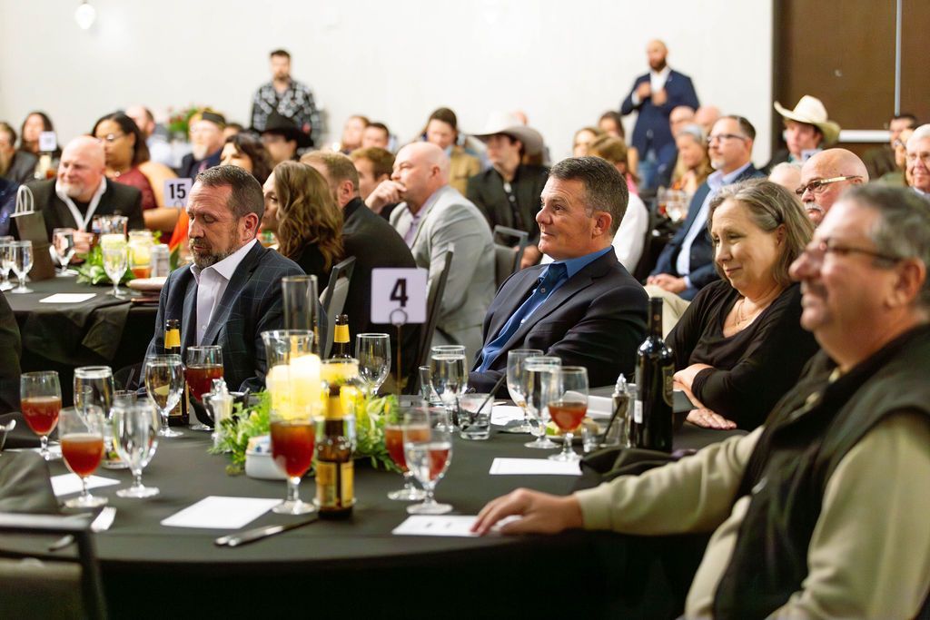 A banquet hall with seated guests at round tables, listening to a presentation.