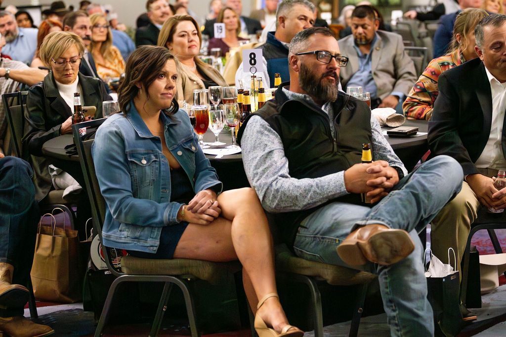 A group of people seated at round tables during an indoor event, focused forward with attentive expressions.