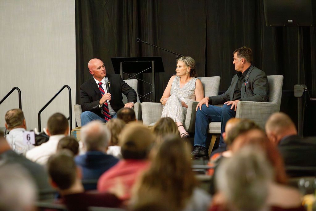 Three people sit on chairs on a stage, addressing an audience during a presentation.