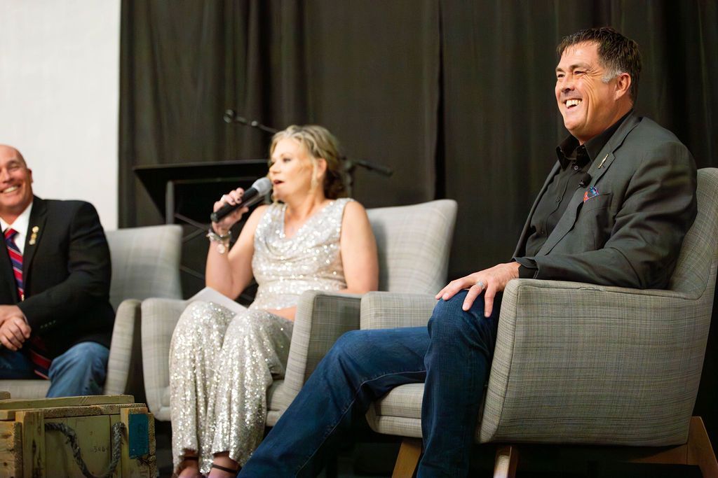 Three people sitting on stage in chairs, with a woman speaking into a microphone and the others smiling.