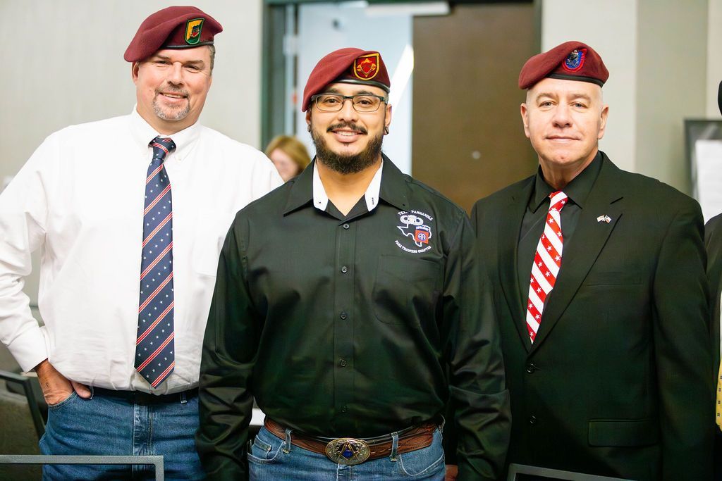 Three people wearing maroon berets stand together indoors, dressed in formal attire including ties and dress shirts.