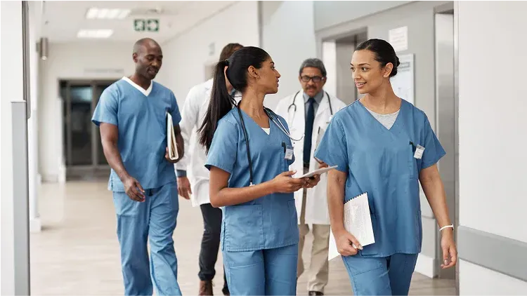 Medical professionals in blue scrubs walking in a hospital hallway.