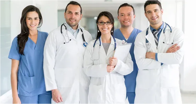 Medical team smiling in a brightly lit hallway; scrubs and white coats.