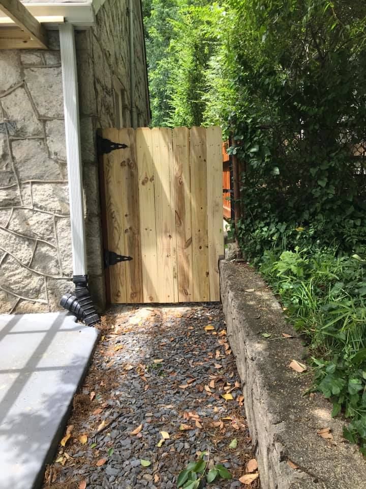 Wooden gate with black hinges set between stone wall and greenery.