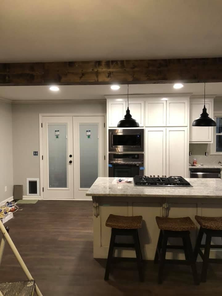 Kitchen with white cabinets, island with stools, and pendant lights. Frosted glass doors and a dark wood beam.