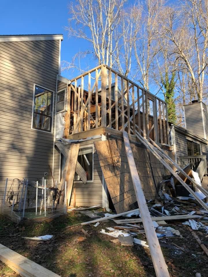 Deck construction on a house: unfinished wooden structure with exposed framing, surrounding trees, and scattered debris.