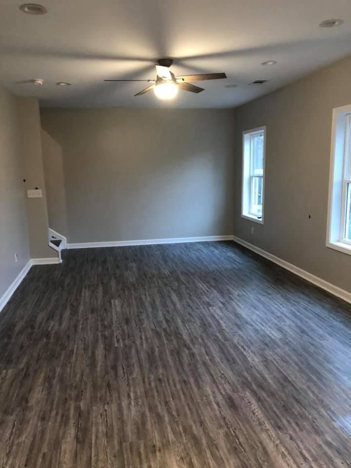 Empty living room with wood-look flooring, light gray walls, ceiling fan, and two windows.