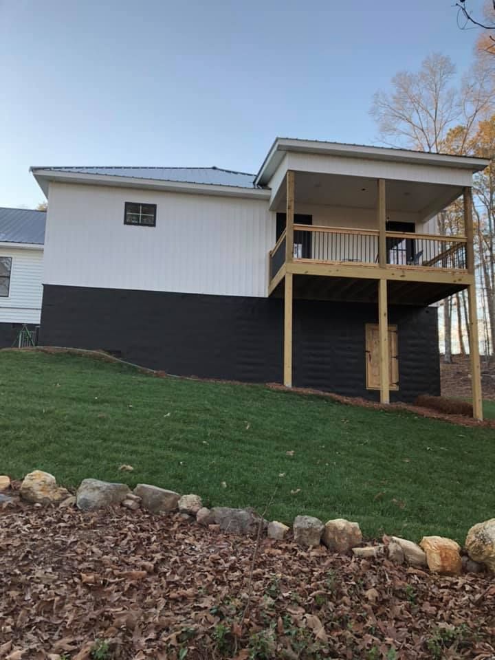 Side view of a two-story house with white upper walls, dark lower walls, and a wooden deck.