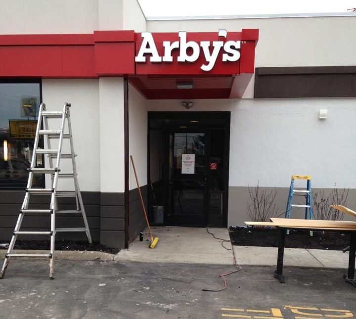 Exterior of an Arby's restaurant with a ladder, tools, and a closed entrance, likely under construction.