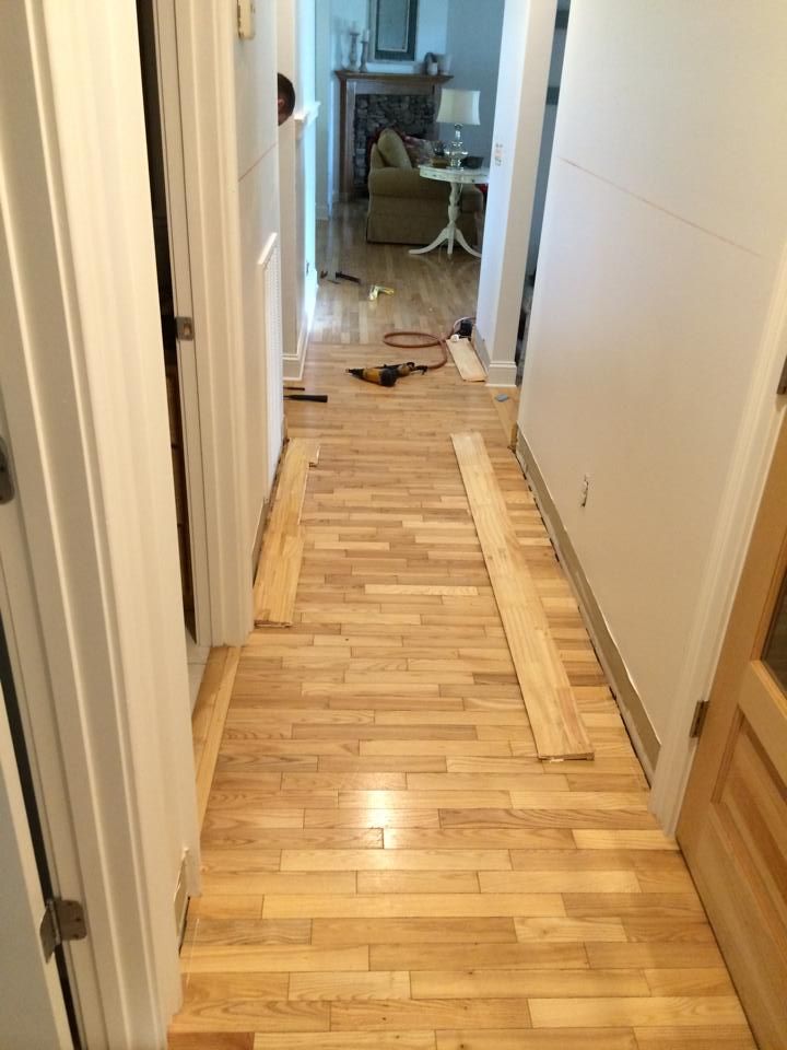 Hallway with wooden floor, boards laid out, tools present, and a view into a living room.
