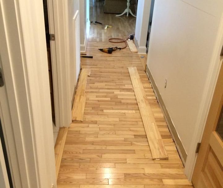 Hallway with hardwood floor being renovated; wood planks and tools on the floor.