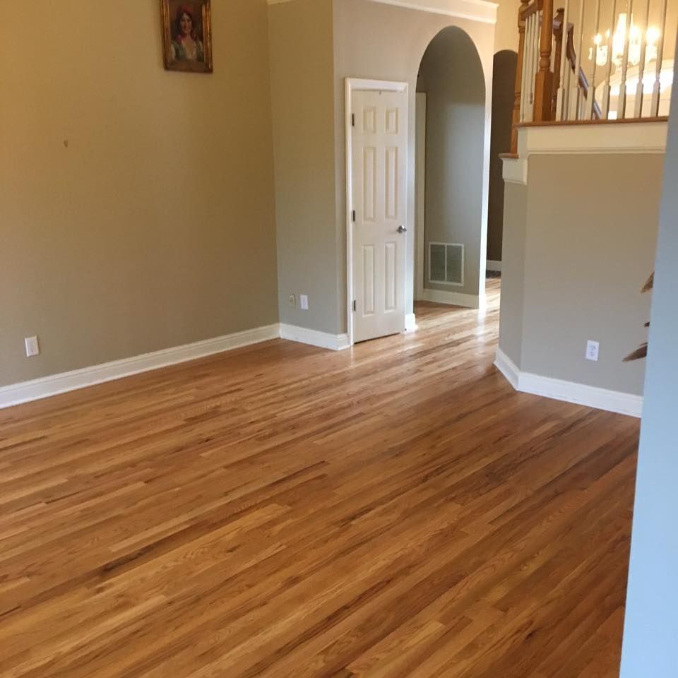 Hardwood floors in a room with tan walls, a white door, and an arched doorway leading to another room.