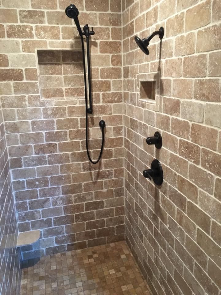 Shower with tan brick-style tile walls, dark fixtures, and built-in shelf.