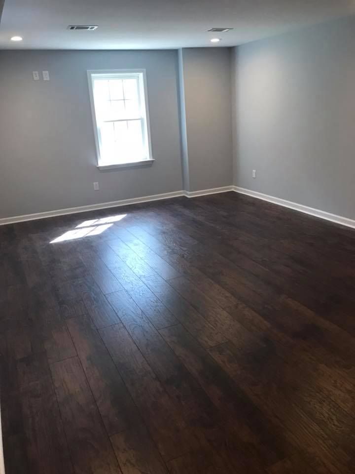 Empty room with dark wood floor, gray walls, white trim, and a window.