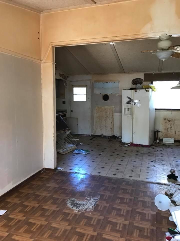 Interior view of a damaged home with debris on the floors. Visible are a kitchen and living room.