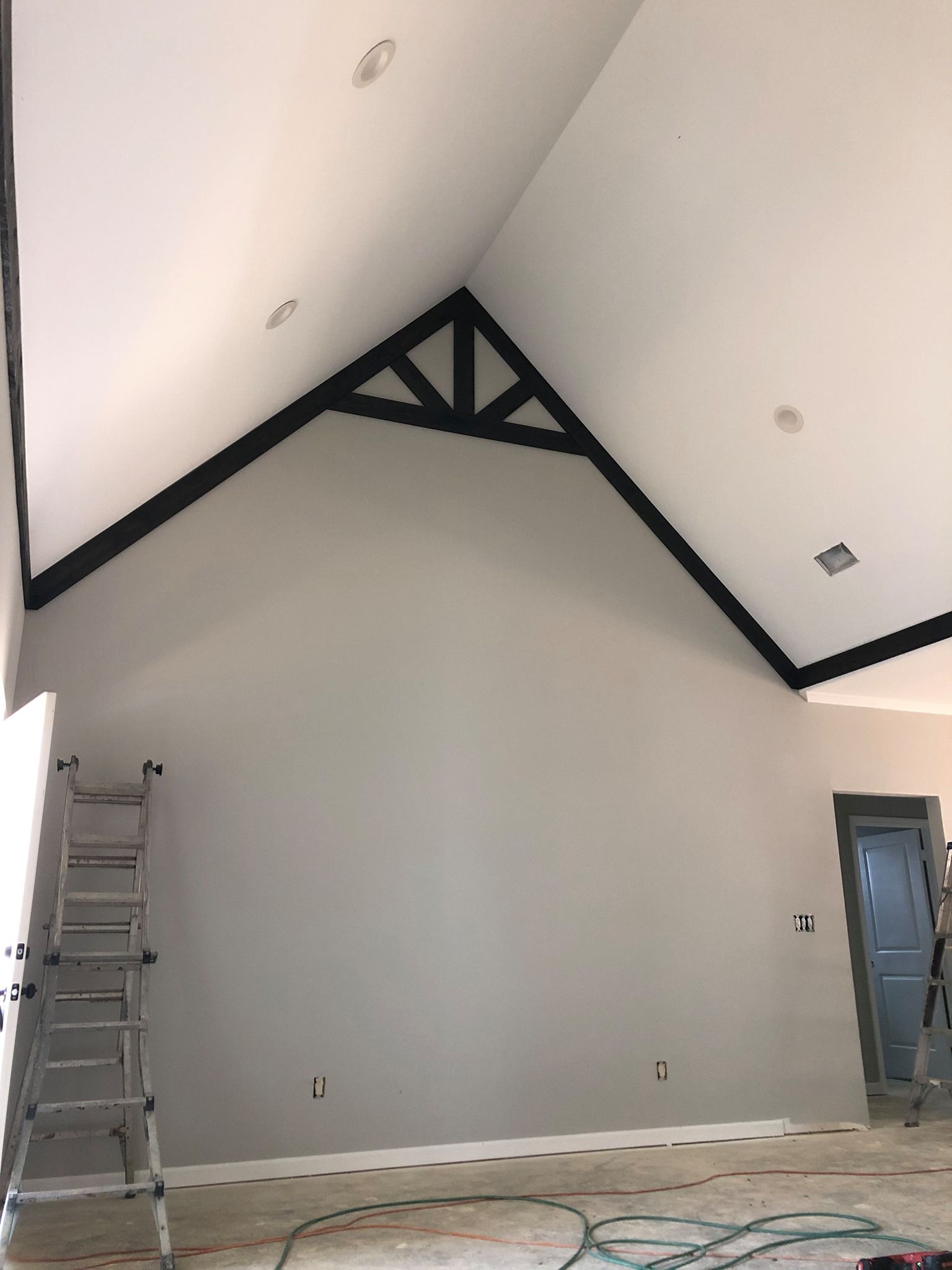 Interior view of a room with a high, slanted ceiling, painted white and gray, with a black truss.