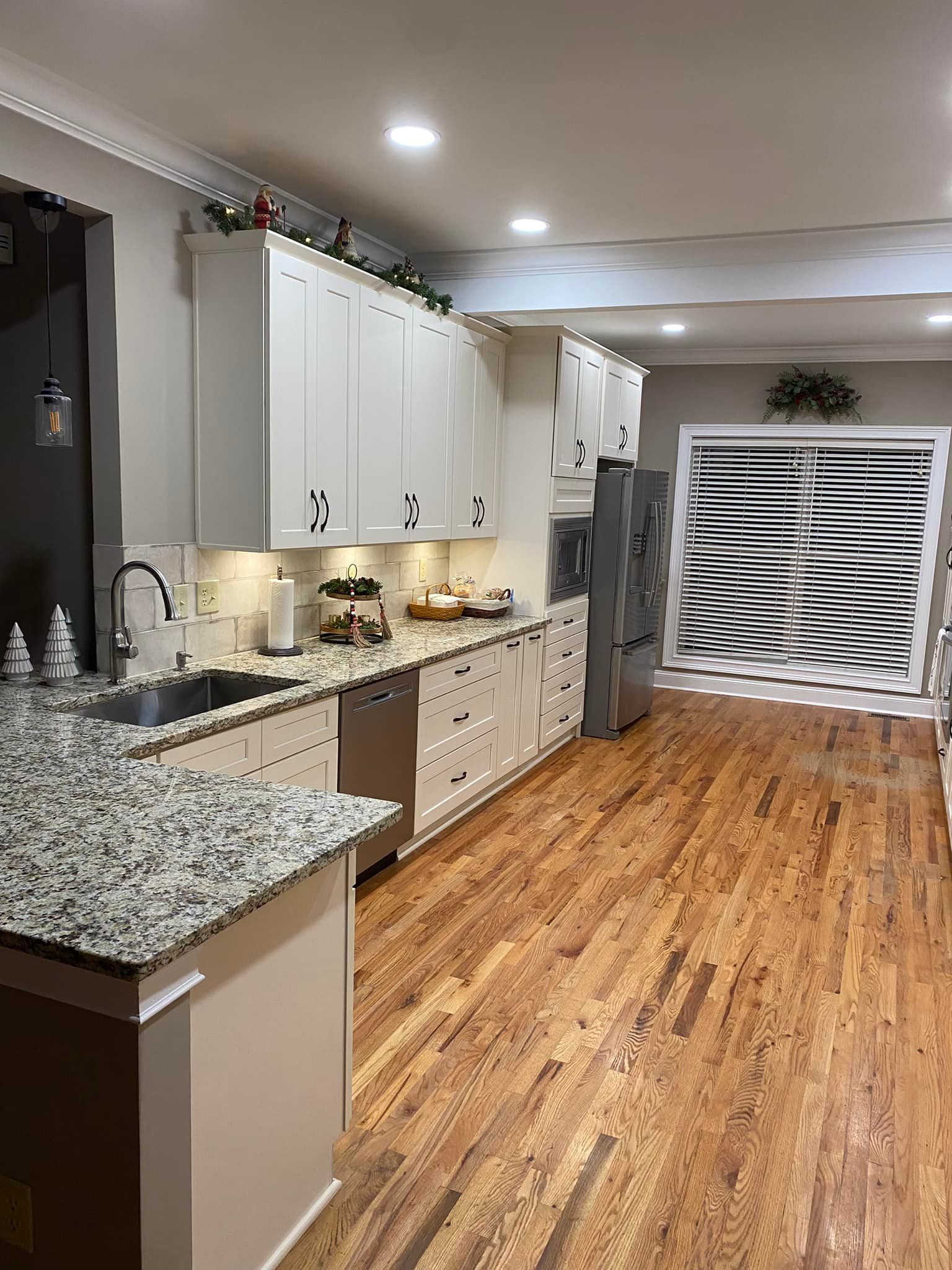 Bright kitchen with white cabinets, granite countertops, stainless steel appliances, and wooden floors.